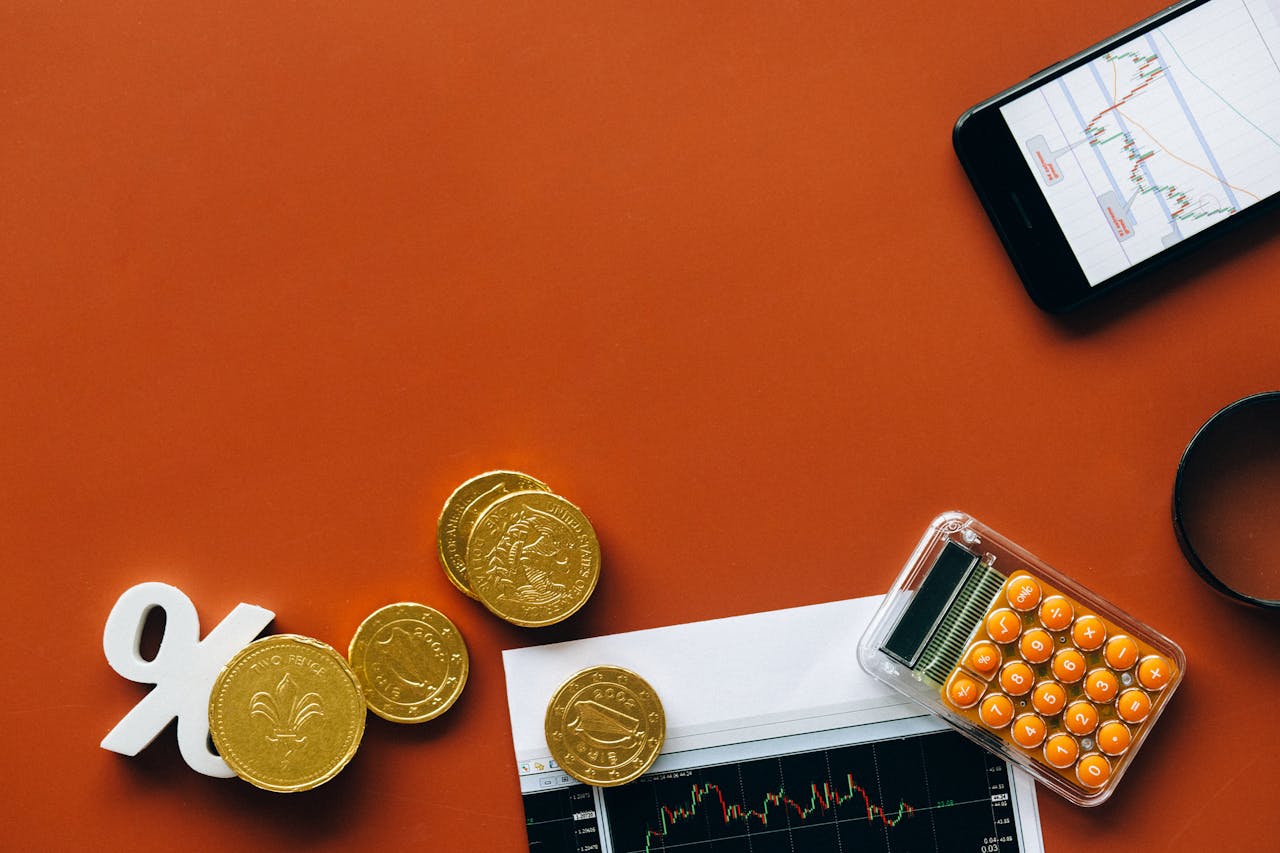 Flat lay showing coins, calculator, and charts on a red background for financial analysis and business concepts.